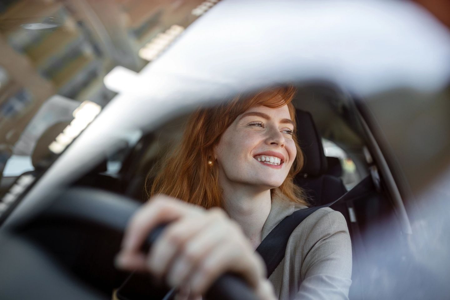 Woman smiling while driving a car, seen from the passenger side.
