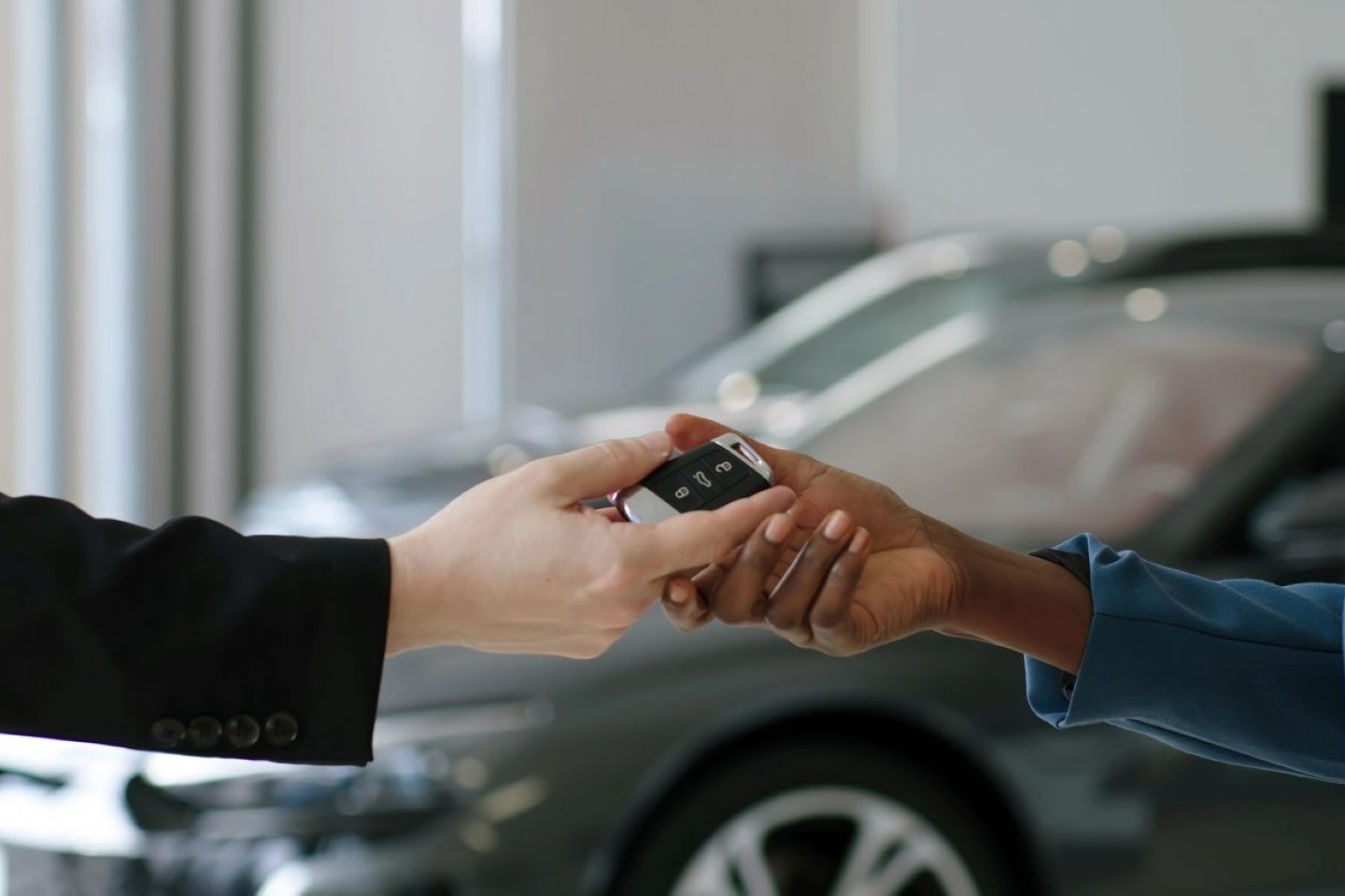 Two people exchanging a car key fob, with a blurred car in the background.